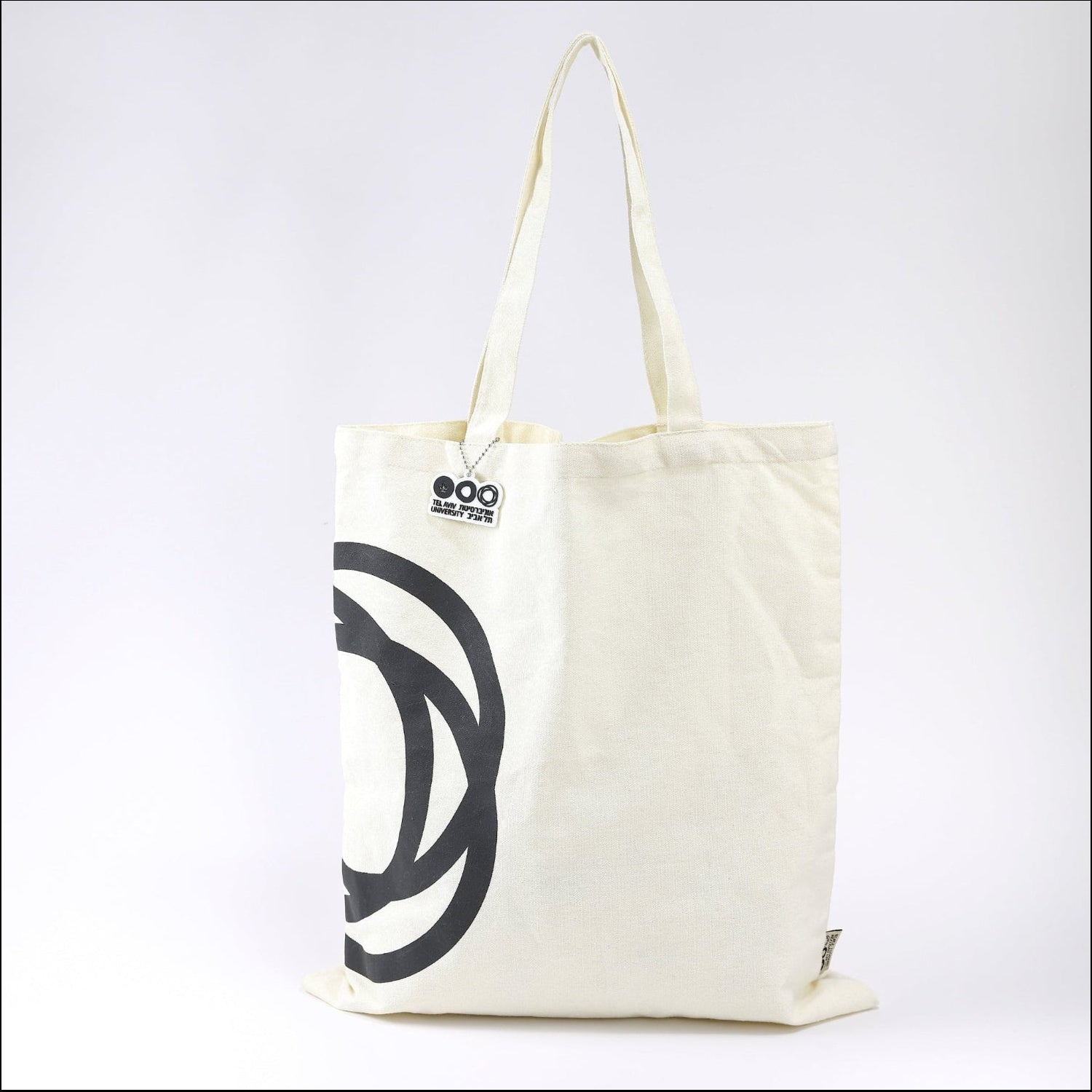 A beige cotton tote bag with a large black graphic design on the front side, featuring long handles.